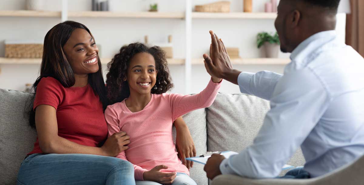A Black American mother and daughter exchange a high-five with a Black American male therapist.