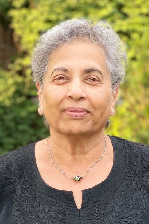 A woman of south-Asian descent, with short gray hair. She is wearing a black blouse and smiling.