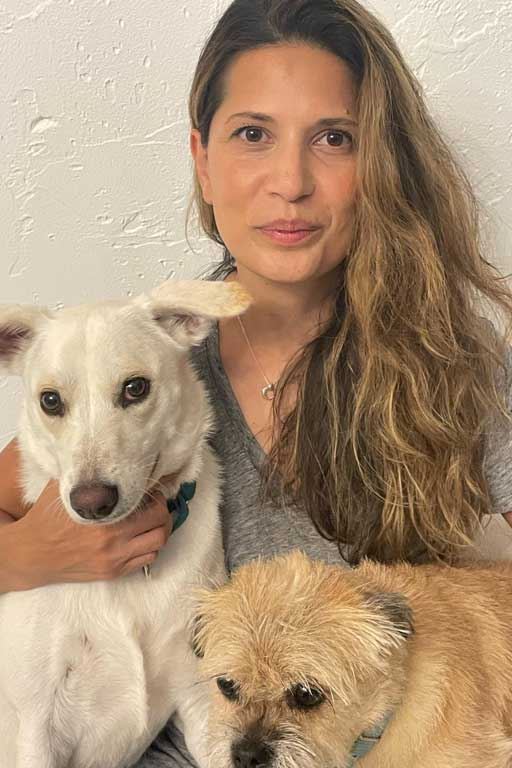 Shavaun Tucker is a light skinned woman with dark blond, long hair. She is posing with a large white dog and a small carmel-colored dog.