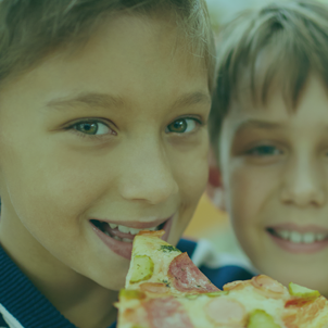 Two Caucasian boys enjoy slices of pizza.