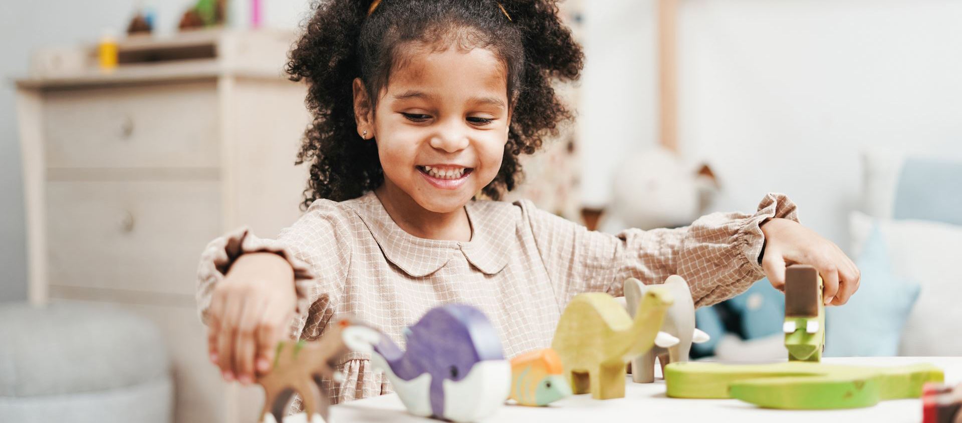 A preschool-aged Black American girl plays with wooden dinosaurs at a table.