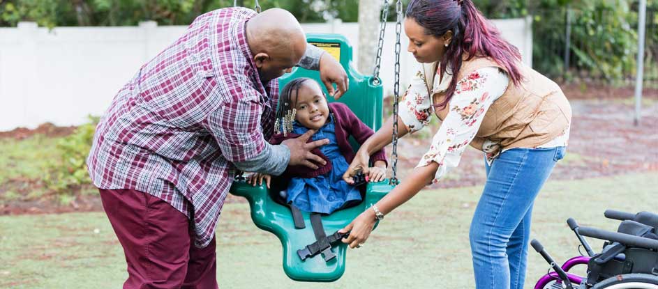 Black American parents push their daughter in an adapted swing at a playground