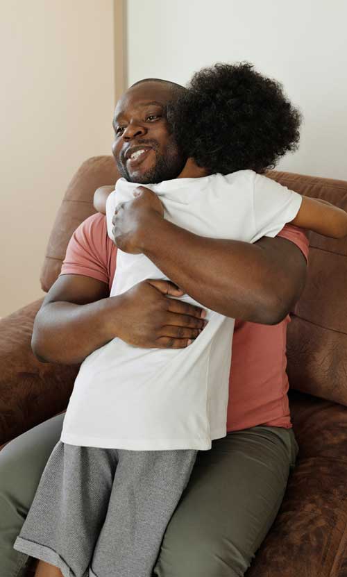 A Black American father and son embrace warmly.