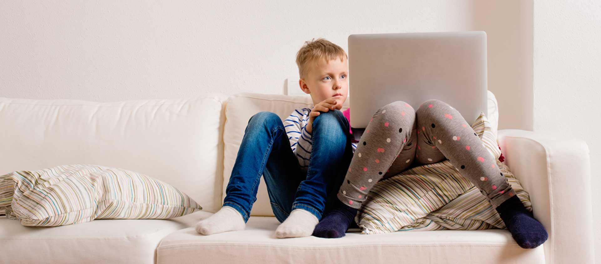 Two children sit on a sofa, transfixed with a laptop.