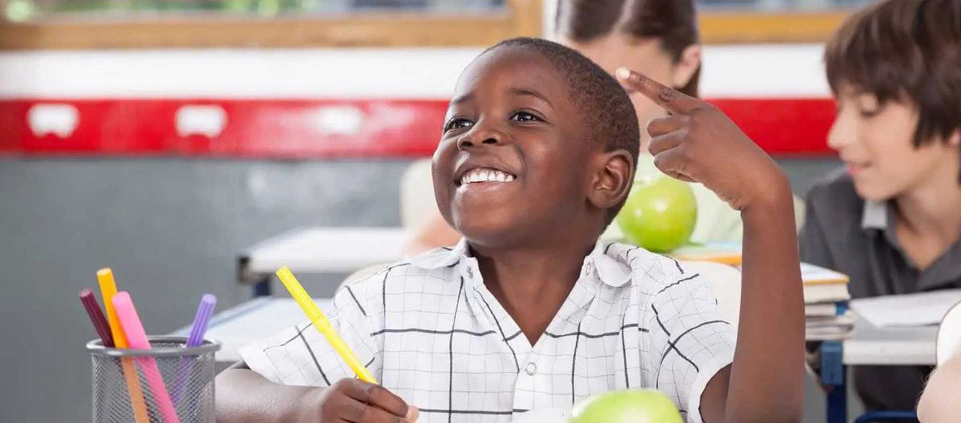 A Black American boy at a desck in school. He is smiling.