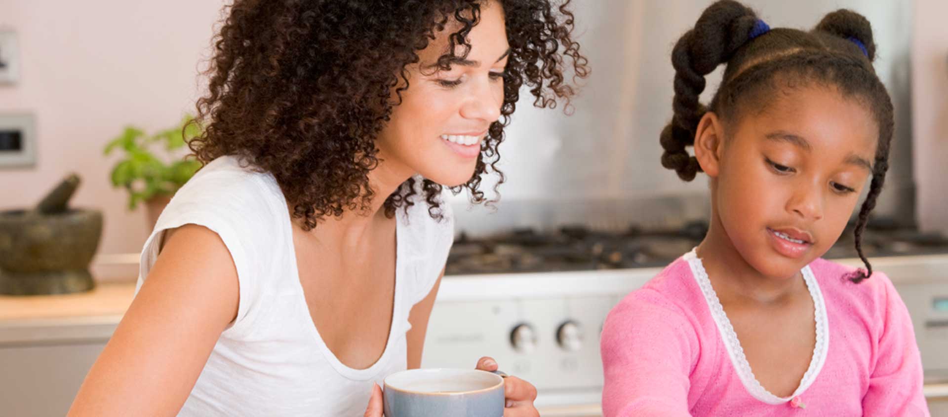 A smiling Black American mother and daughter together at a kitchen table.