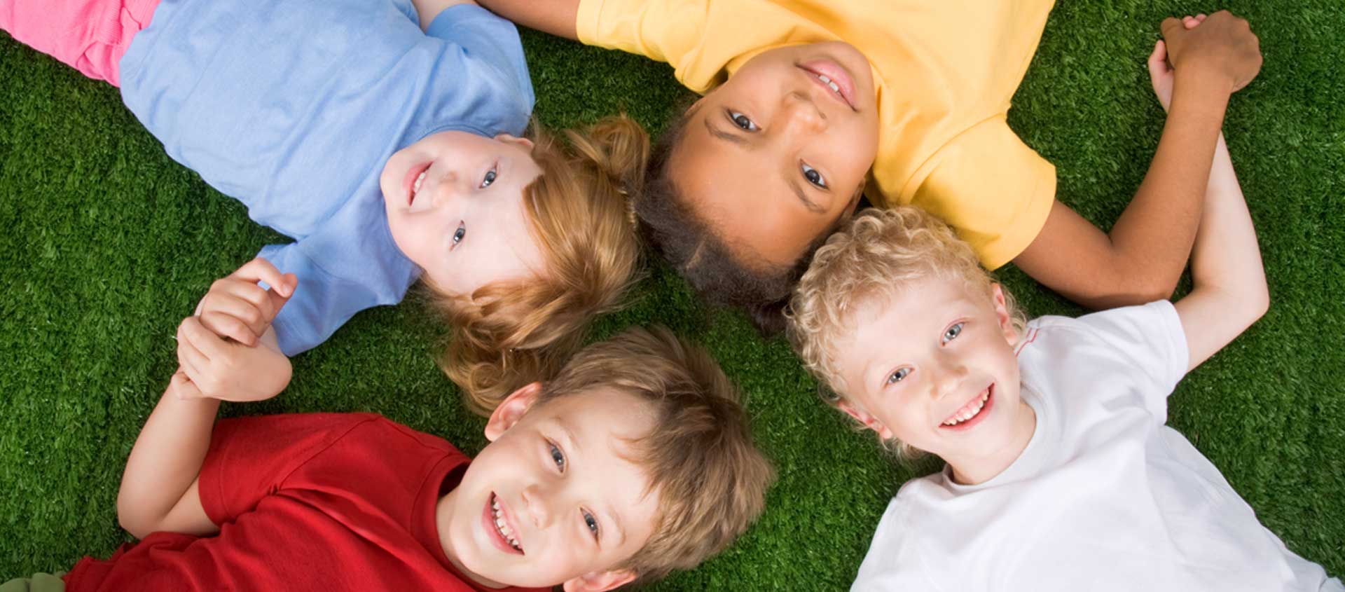 A diverse group of four children lay in the grass holding hands