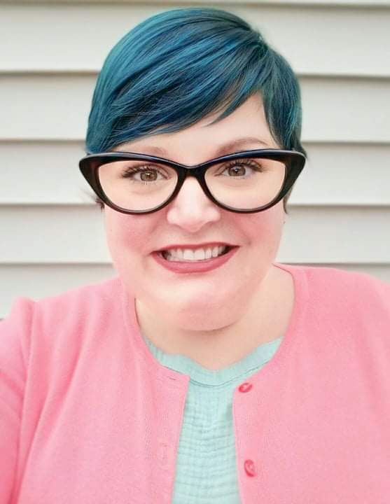 A Caucasian woman with short, blue dyed hair and glasses.